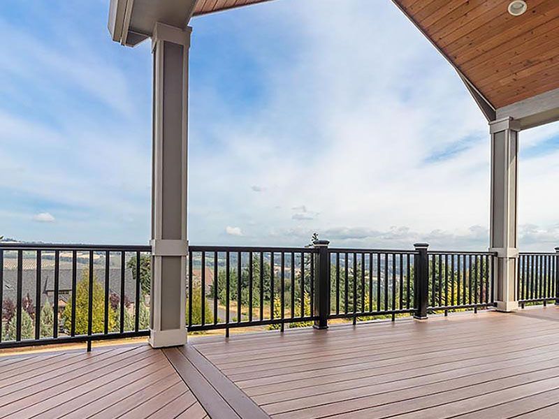 Spacious wooden deck with black railing overlooking a distant city skyline under a cloudy sky