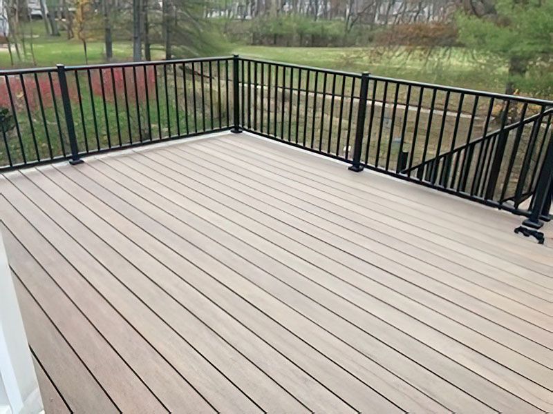 Empty beige deck with black railing overlooking a grassy yard and trees