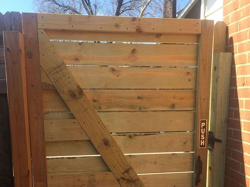 Wooden fence gate with diagonal brace and latch, viewed outdoors in daylight.