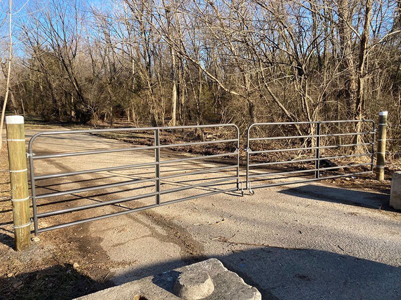 Closed metal gate across a dirt road in a wooded area under bare winter trees