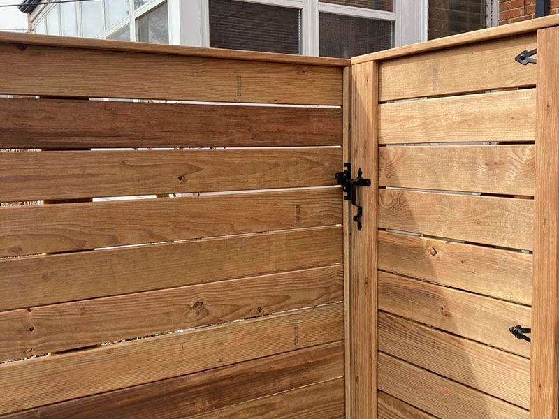 Wooden privacy fence corner with black latch and house windows behind it