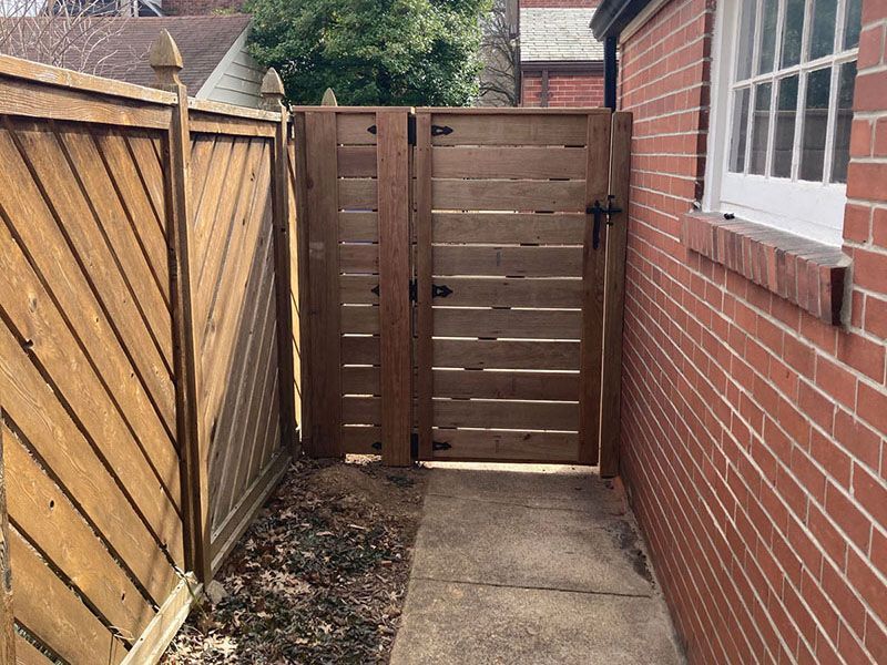 Narrow backyard path beside a brick house, leading to a wooden gate and fence.