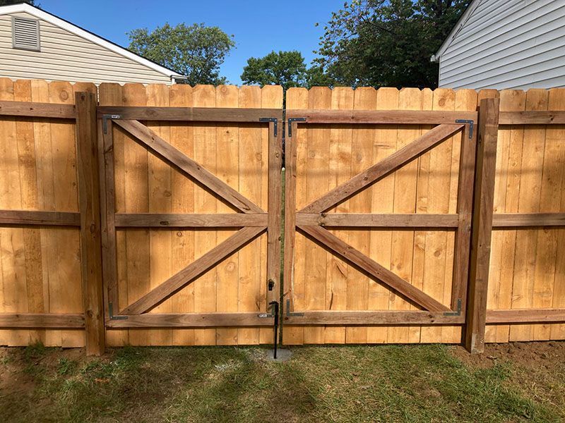 Wooden backyard fence with double gates and diagonal braces, set between two houses under a blue sky