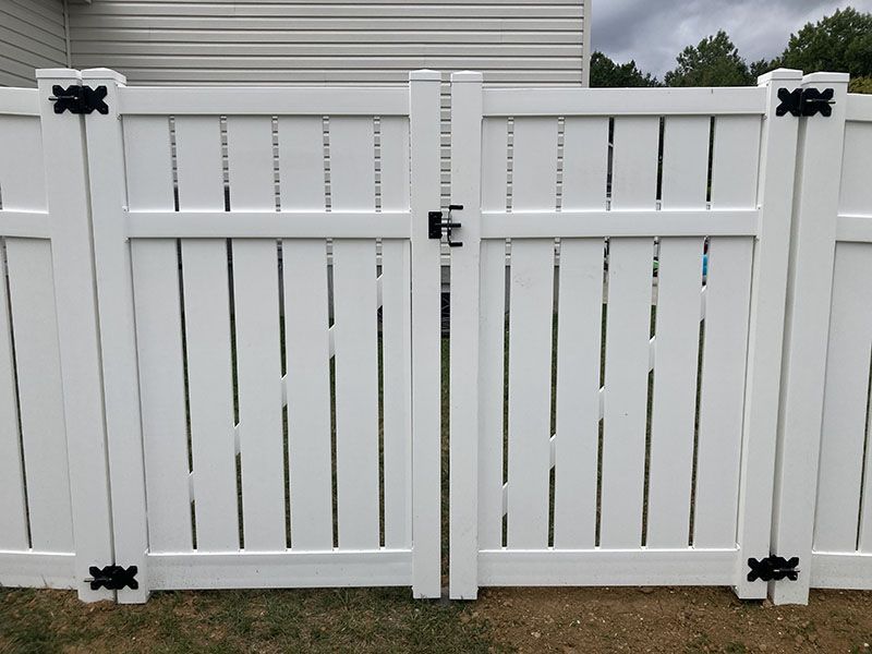 White vinyl double gate with black decorative hinges in front of a house fence
