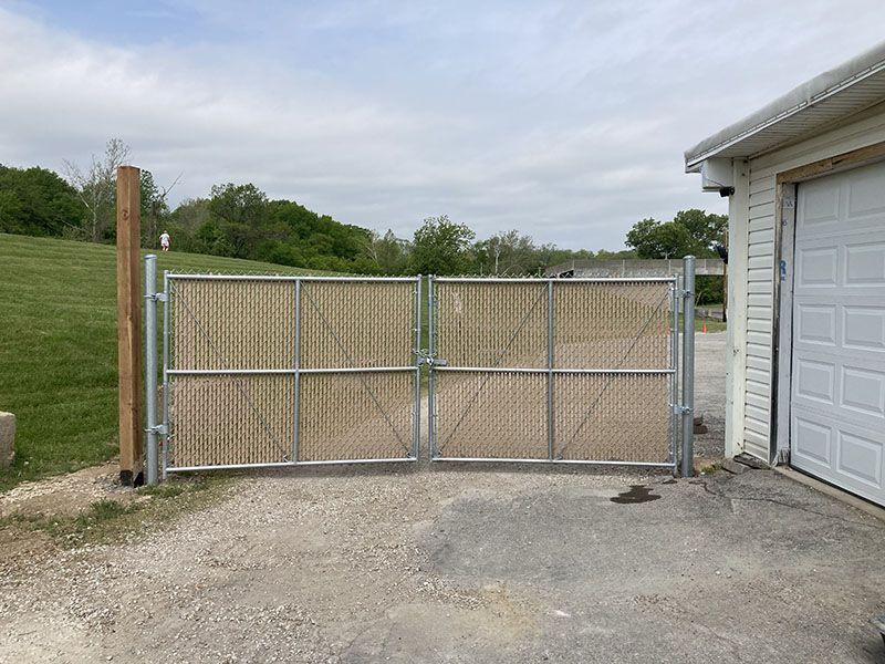 Wooden double gate in a gravel driveway beside a white garage, with grass and trees in the background
