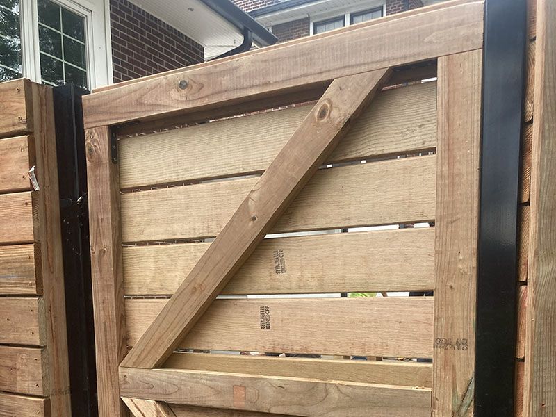 Wooden backyard gate with diagonal brace, attached to a fence and open slightly at the top