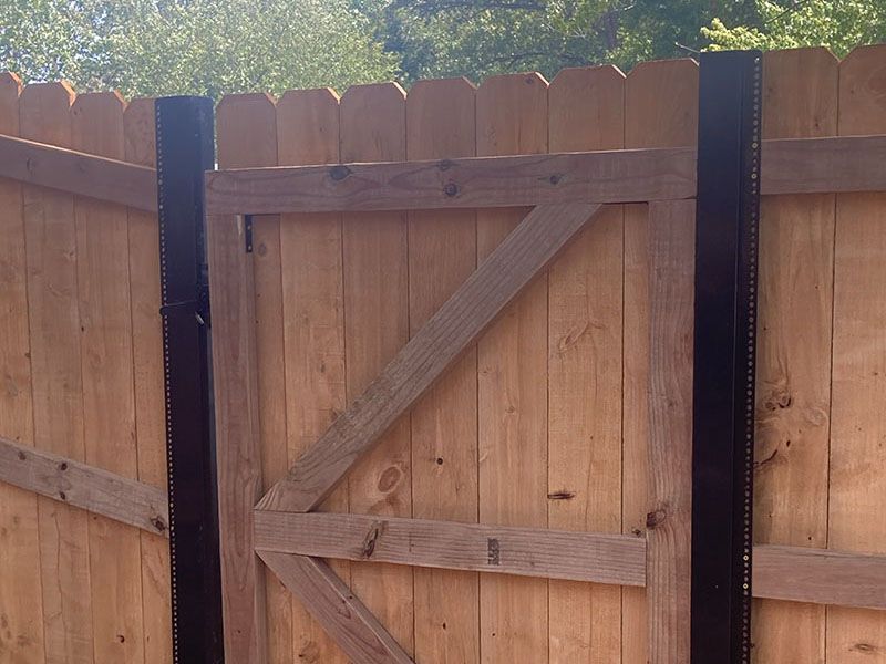 Wooden garden gate with diagonal bracing, set in a brown fence under daylight.