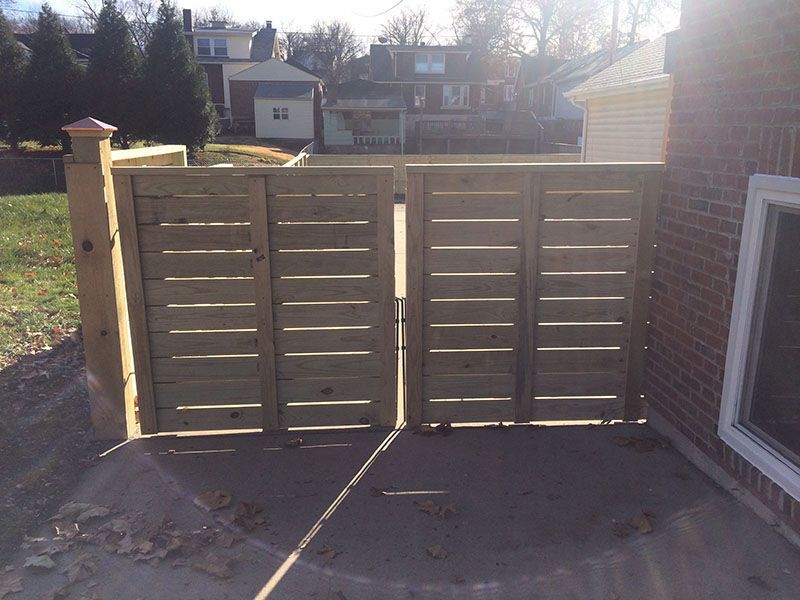 Wooden privacy fence panels beside a house, with sunlight casting shadows on the ground.