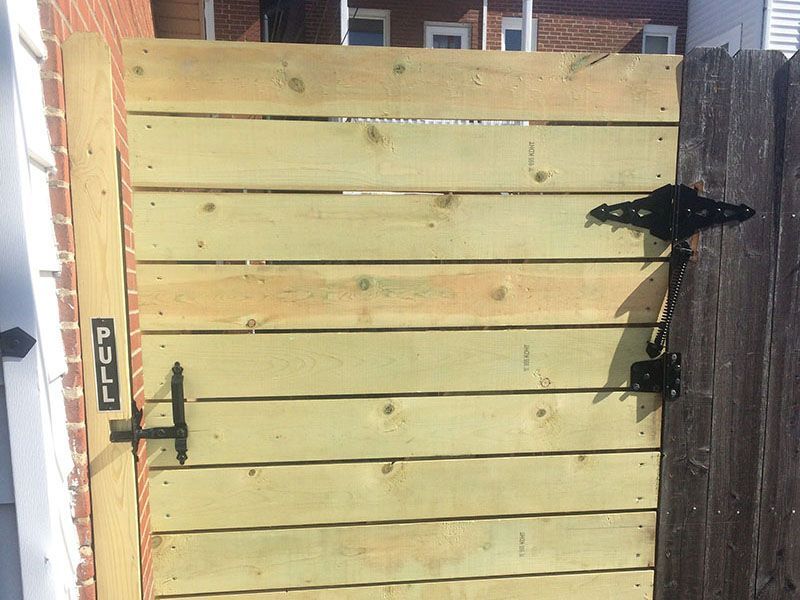 Yellow wooden gate with black handle and latch, partly open beside a brick wall and fence