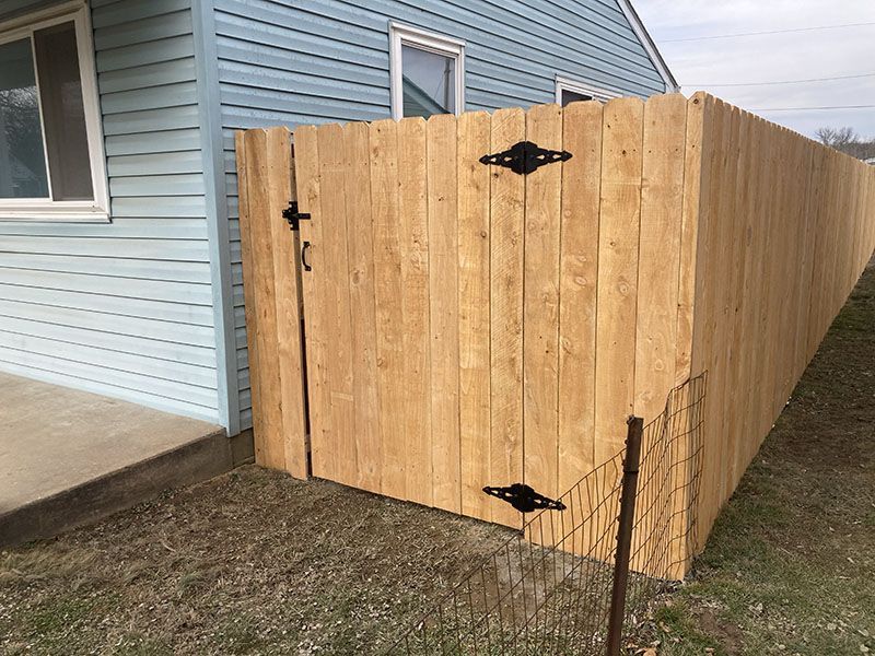 Wooden fenced side yard gate with black hinges beside a light blue house.