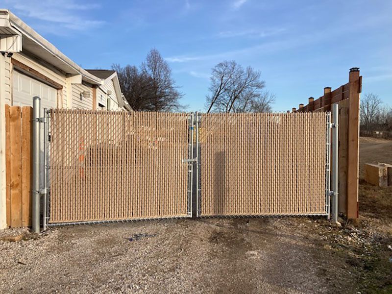 Wooden lattice double gate across a gravel driveway beside beige buildings under a clear sky