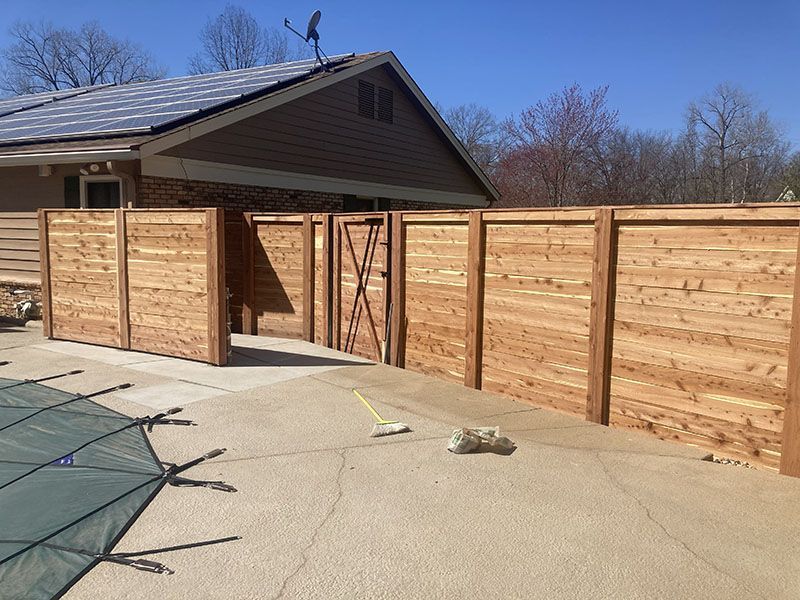 Wooden backyard fence with an open gate beside a house and concrete patio.