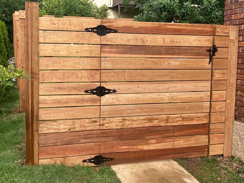 Wooden driveway gate with black hinges and latch, set in a garden fence