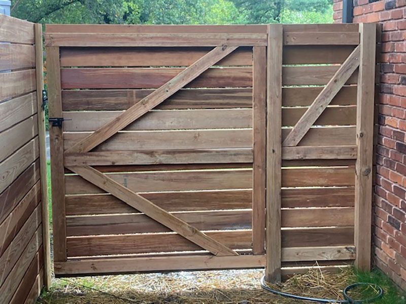 Wooden garden gate with diagonal bracing, set between brick walls and trees beyond