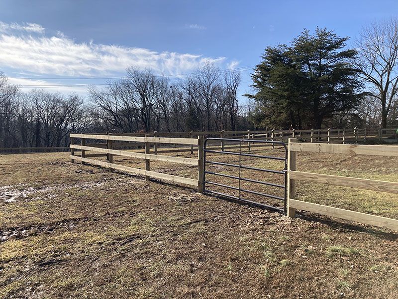 Wooden fence and metal gate in a grassy field under a partly cloudy sky
