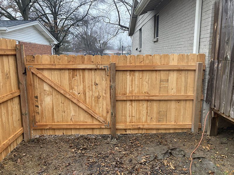 New wooden privacy fence gate between a house and side fence, with muddy ground in front