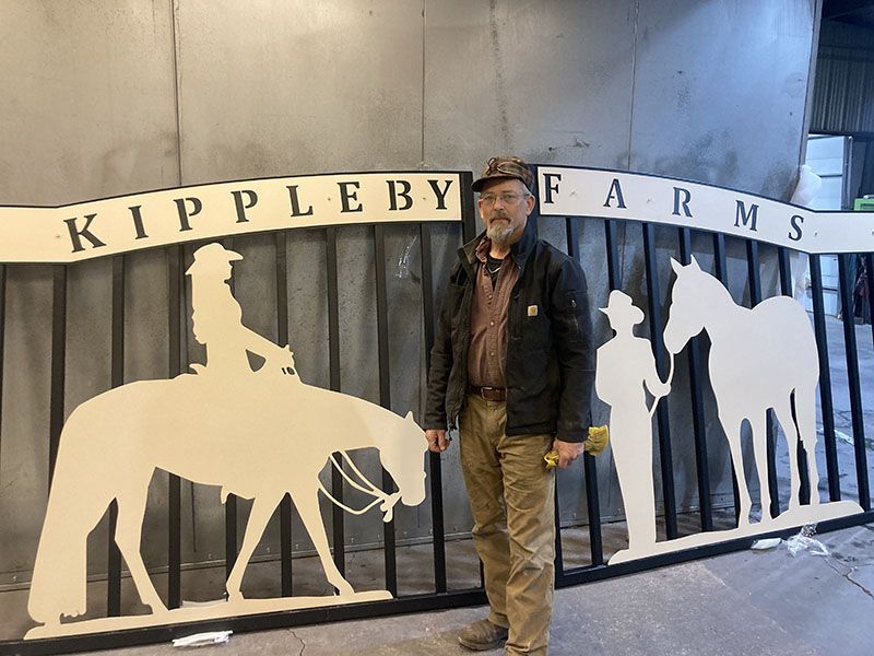 Man standing beside a Kippleby Farms sign with cowboy and horse silhouettes.