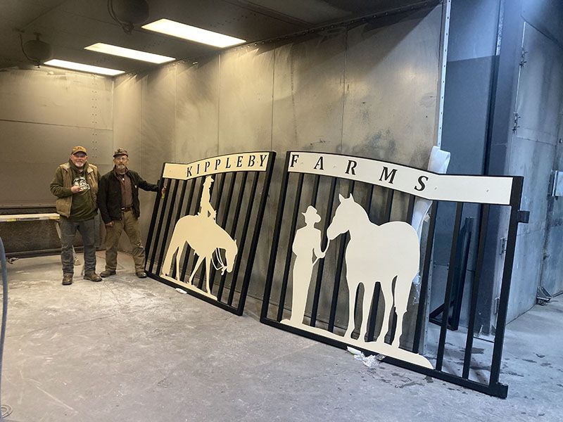 Two people beside a black-and-white cattle gate sign reading “EMLOY FARMS” in a concrete room