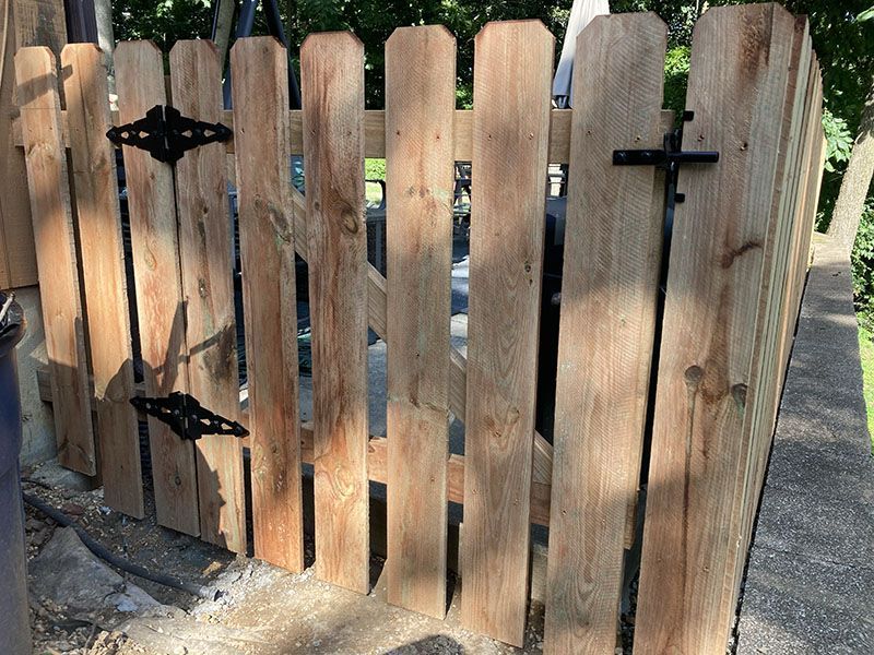 Wooden picket gate with black metal hinges, viewed from the front outdoors