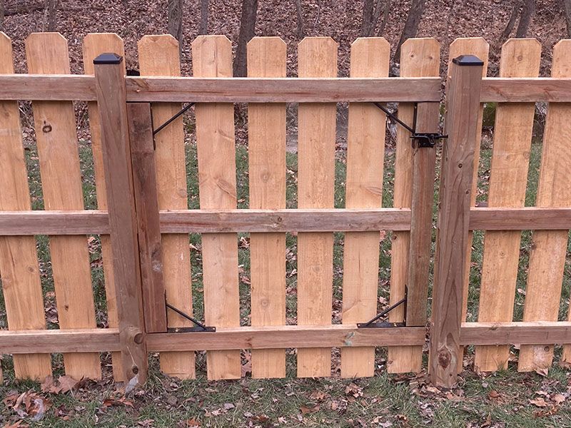 Wooden fence gate with black latch, framed by a brown picket fence and leaf-covered ground