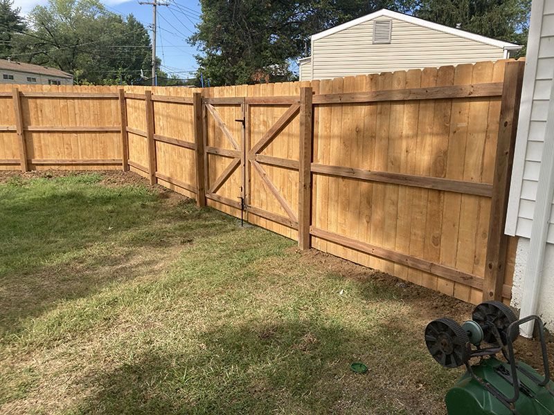 Wooden privacy fence with a double gate enclosing a grassy backyard under a clear sky