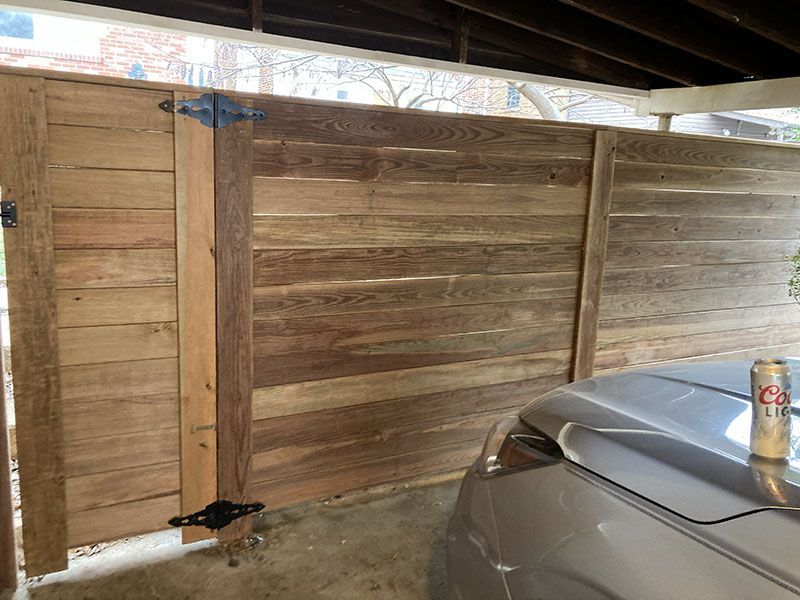 Wooden fence panels beside a silver car under a roof, with a can resting on the car hood.