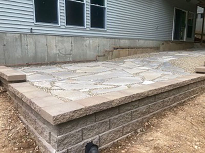 Stone patio with a raised concrete edge beside a house foundation