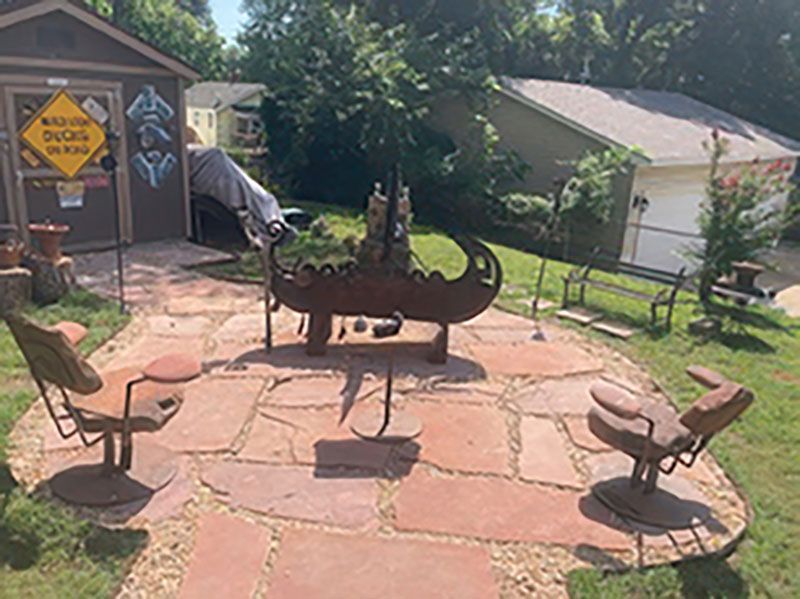 Outdoor patio with animal-shaped metal sculptures and stone paving beside a building and garden.