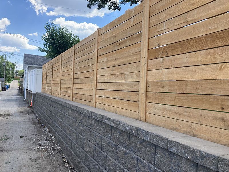 Wooden privacy fence atop a gray cinder block wall along a narrow alley under a cloudy sky