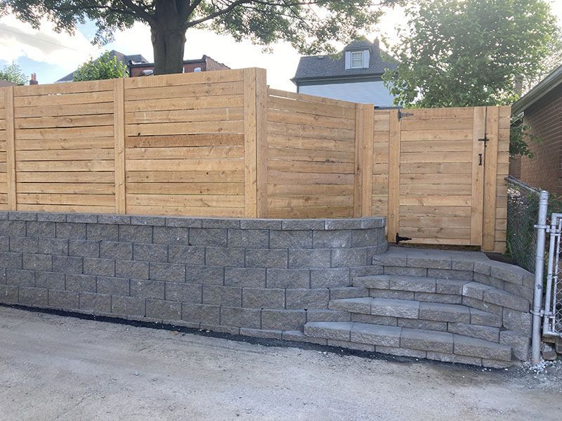Wooden privacy fence atop a gray stone retaining wall and steps beside a driveway