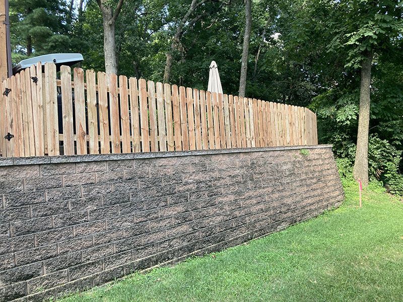 Stone retaining wall with light wooden fence and patio umbrellas along a wooded hillside