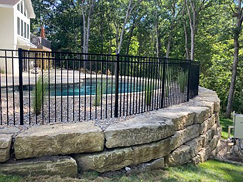 White vinyl double gate with black decorative hinges and latch in front of a white fence and house siding