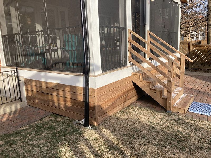 Wooden steps and porch ramp leading to a screened-in sunroom in a backyard.