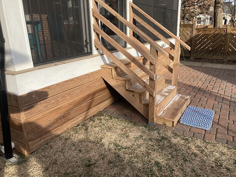 Wooden accessibility ramp with railings beside a house entrance and brick walkway