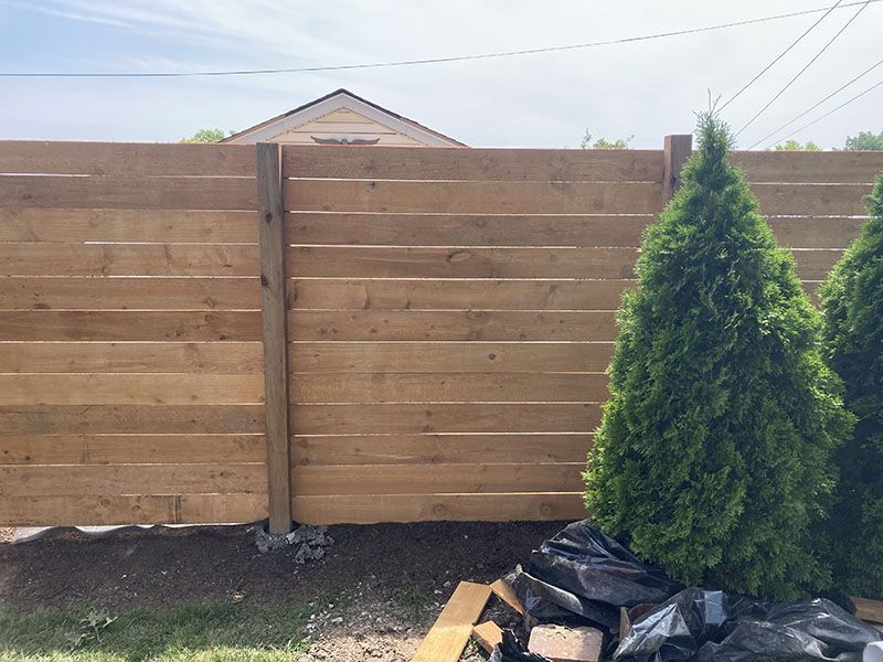 Wooden backyard fence with a small evergreen tree and landscaping materials in front