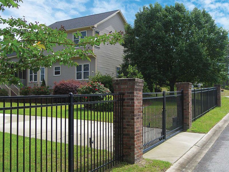 Suburban house with manicured lawn and black metal fence along the sidewalk