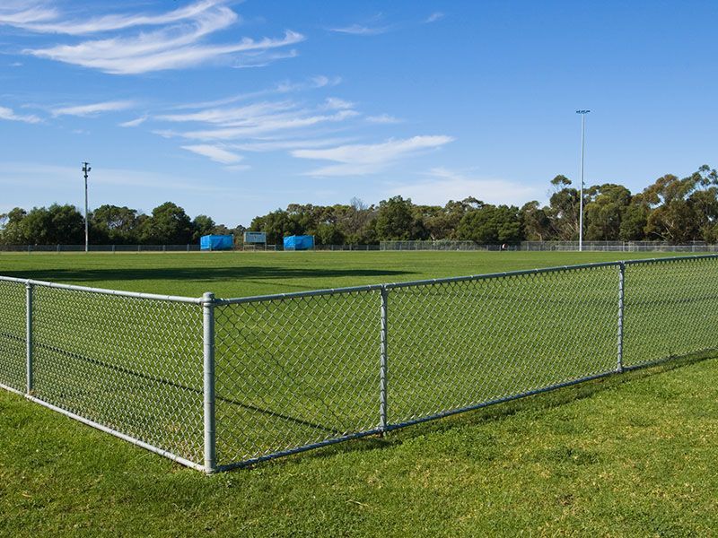 Chain-link fence around a grassy sports field under a blue sky.