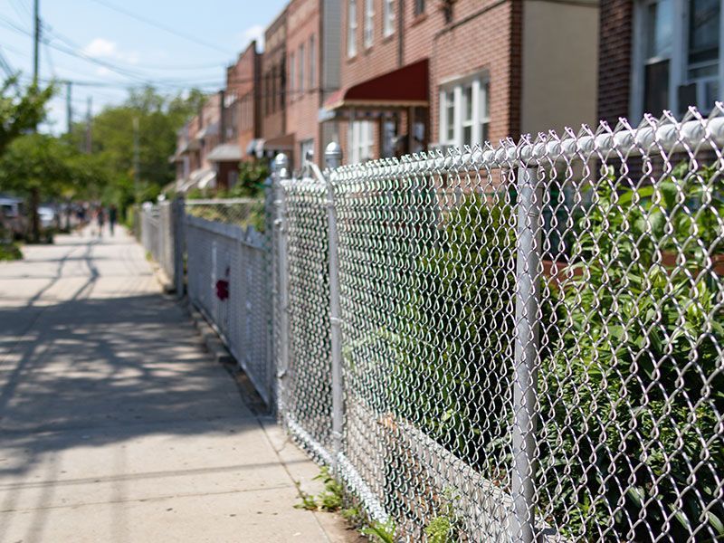 Chain-link fence along a sidewalk beside row houses on a sunny residential street