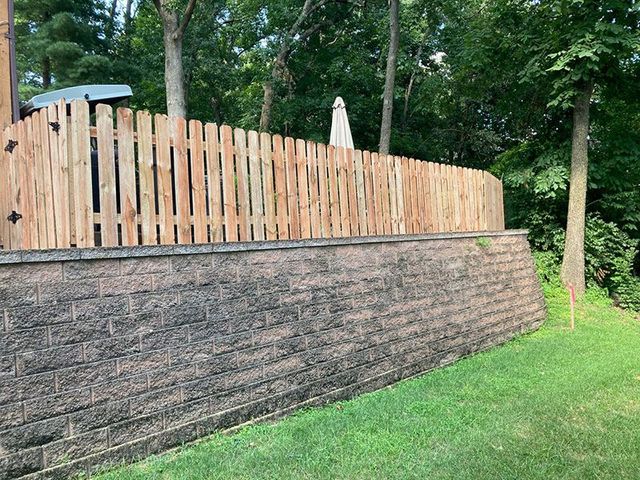 Stone retaining wall beneath a wooden fence in a wooded yard
