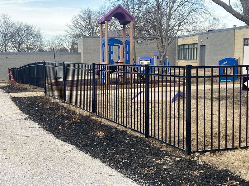Fenced playground with purple play structure and blue slide beside a school building