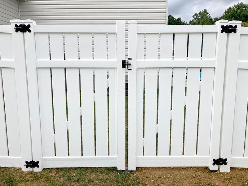 White double gate with black decorative hinges in front of a house fence