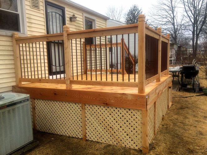 Wooden backyard deck with railing and lattice skirting beside a house, on a cloudy day
