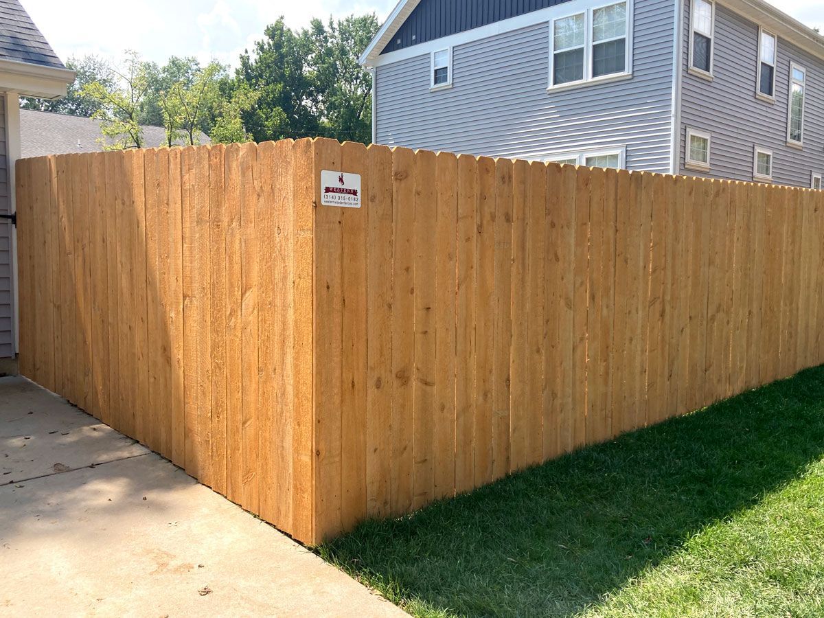 Wooden privacy fence beside a driveway and lawn, with a house in the background.