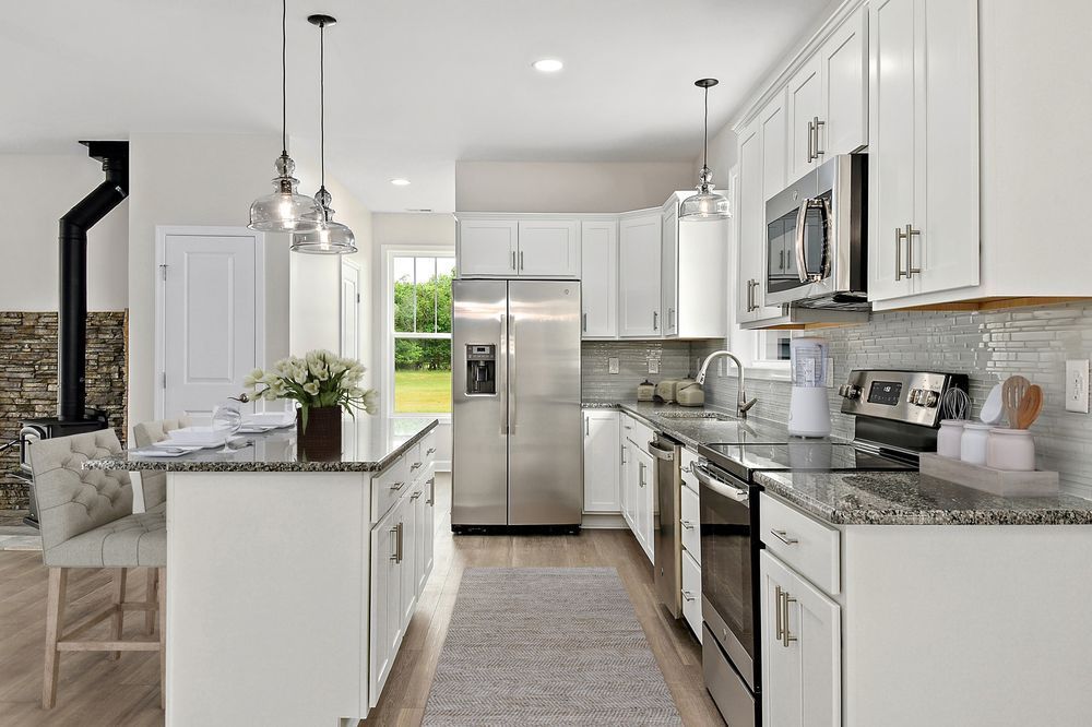 A kitchen with white cabinets, stainless steel appliances, granite counter tops, and a large island.