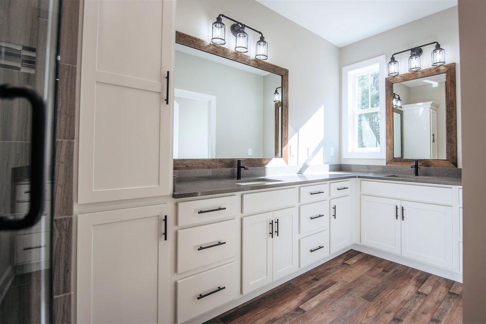 A bathroom with two sinks , two mirrors , and hardwood floors.