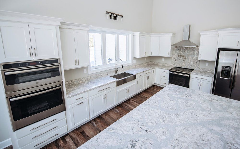 A kitchen with white cabinets , granite counter tops , stainless steel appliances and a large island.