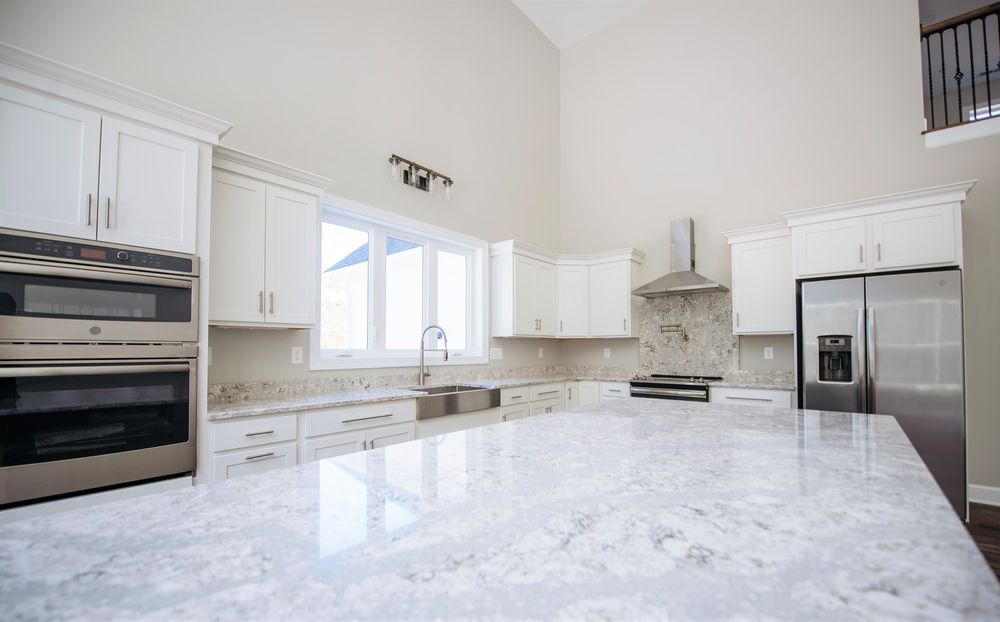 A kitchen with white cabinets, granite counter tops, stainless steel appliances, and a large island.