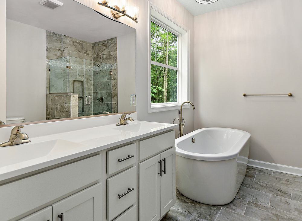 A bathroom with a tub , sink , mirror and window.