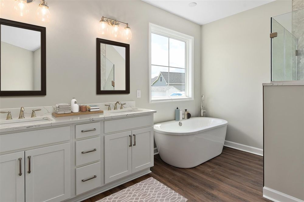 A bathroom with two sinks , a tub , and two mirrors.
