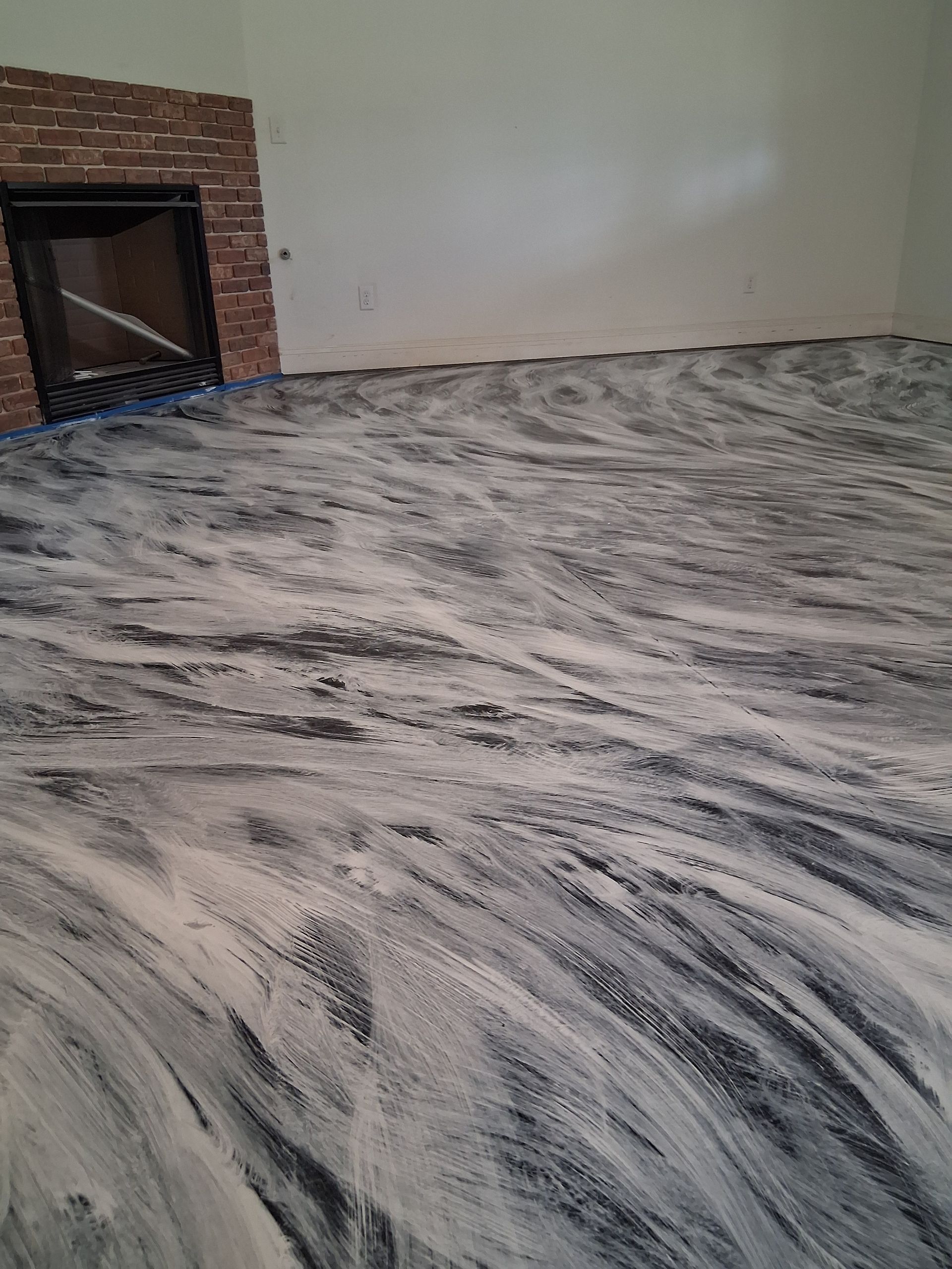 An indoor room featuring a smooth floor with a swirling, marbled gray and white epoxy pattern near a brick fireplace.